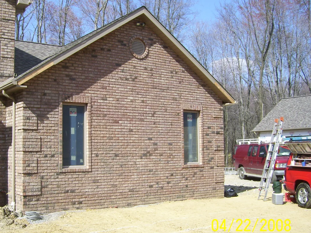 The same gable in April 2008 after the dark units were lightened, the blend reading more evenly around the round vent and the two windows, with an extension ladder and a work van at the right