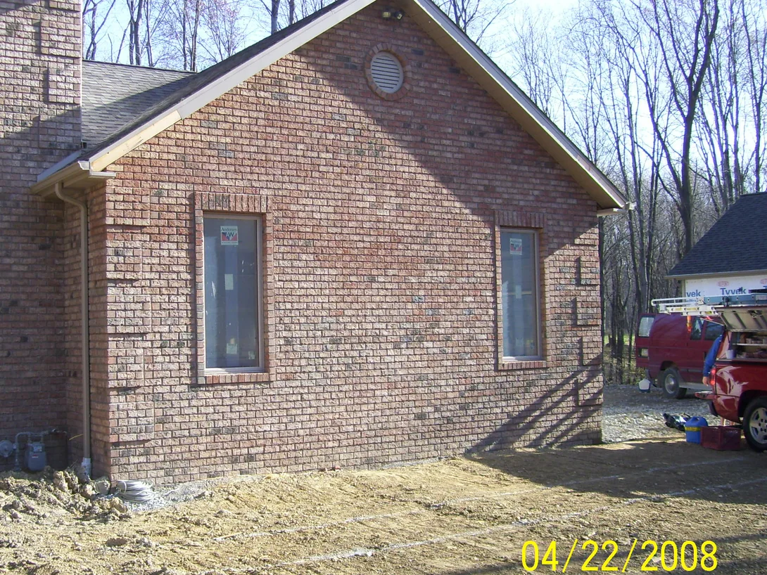 The gable end of the house in April 2008 before staining, a tan and pink brick blend with many dark red units standing out across the wall, the windows still carrying their factory labels and bare ground below
