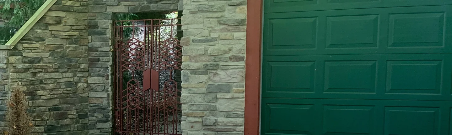 The gated stone entry and green garage door of the Snow Trail home in 2019, burgundy units scattered through grey and tan coursed stone under a red brown fascia