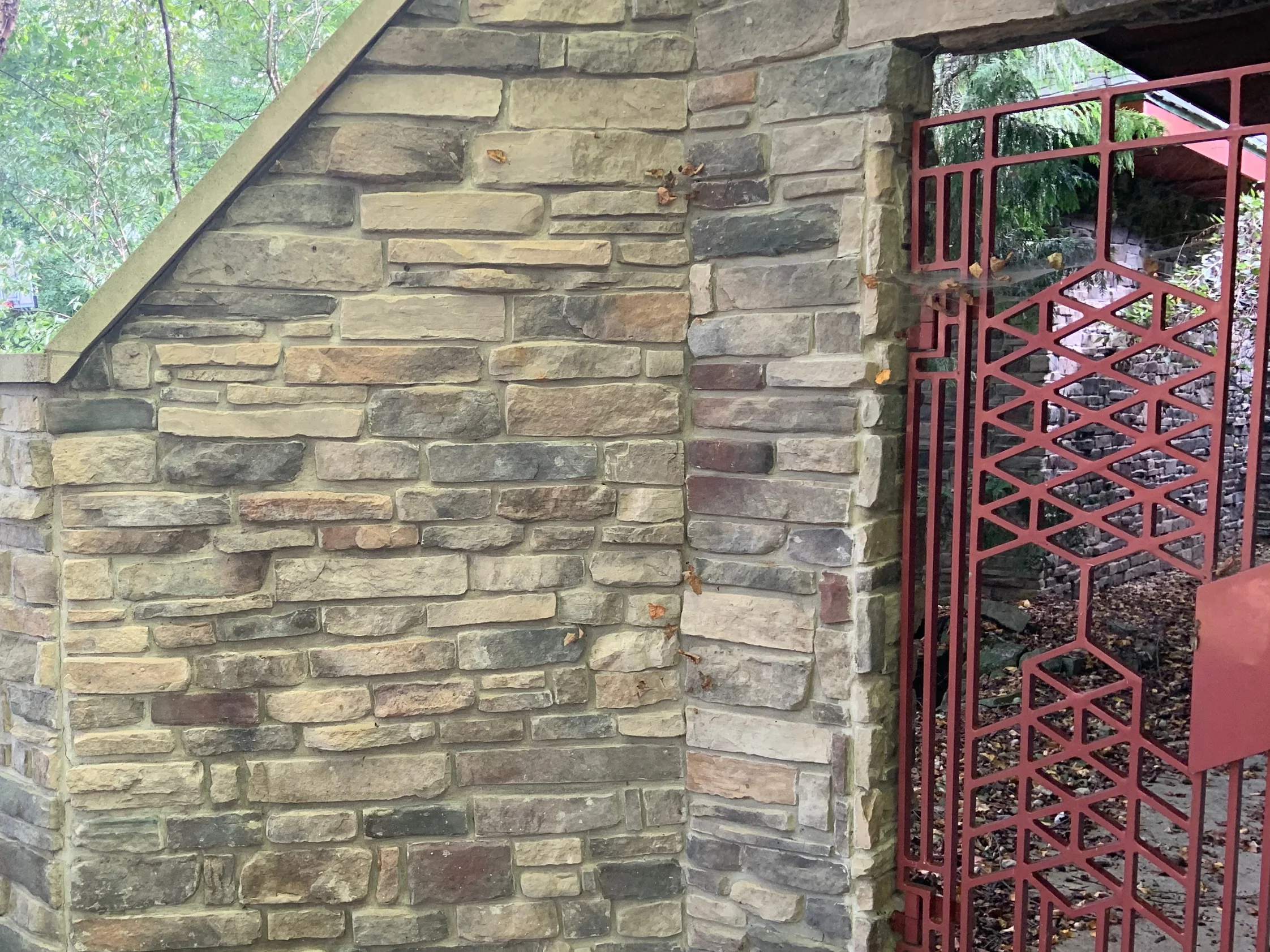 The outside corner of the garden wall at the entry gate in 2019, burgundy units scattered through the tan and grey stone on both faces