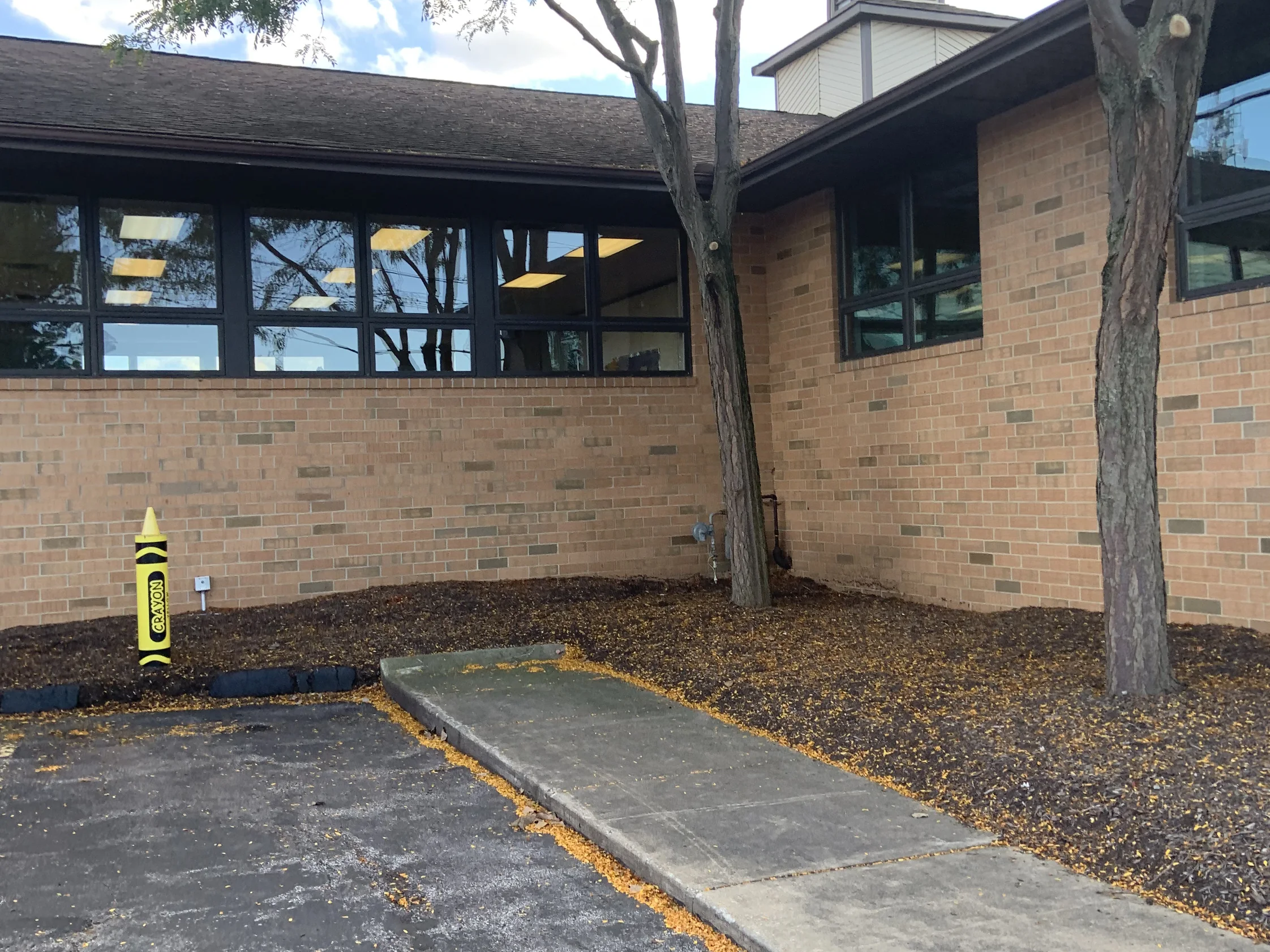 The entry elevation in 2019, stained brick running as one buff and tan range under a band of clerestory windows, a cupola above the roof and a walkway to the door