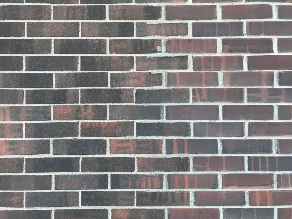 Close view of the wall at the line where two brick faces meet, the texture changing from sanded to smooth while the color runs straight across the join