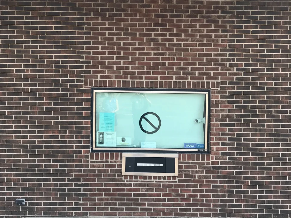 The display case and night deposit bay under the canopy in 2019, the brick running one color across the wall on both sides of the opening
