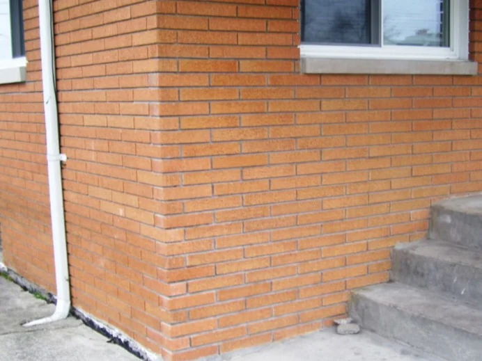 The same corner in 2010 after staining, the replacement brick and its mortar now reading as one range with the original wall from the downspout round to the porch steps