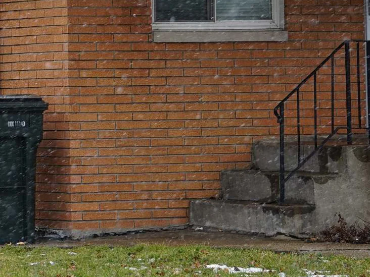 The rebuilt corner at unit scale in 2020, snow blowing across it, the replacement brick and mortar still reading as the wall around them from the window sill down to the steps