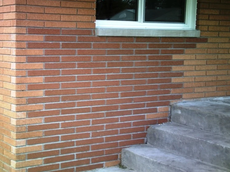 The rebuilt corner of the house in 2010 before staining, the replacement brick below the window reading darker and redder than the orange brick of the original wall on either side