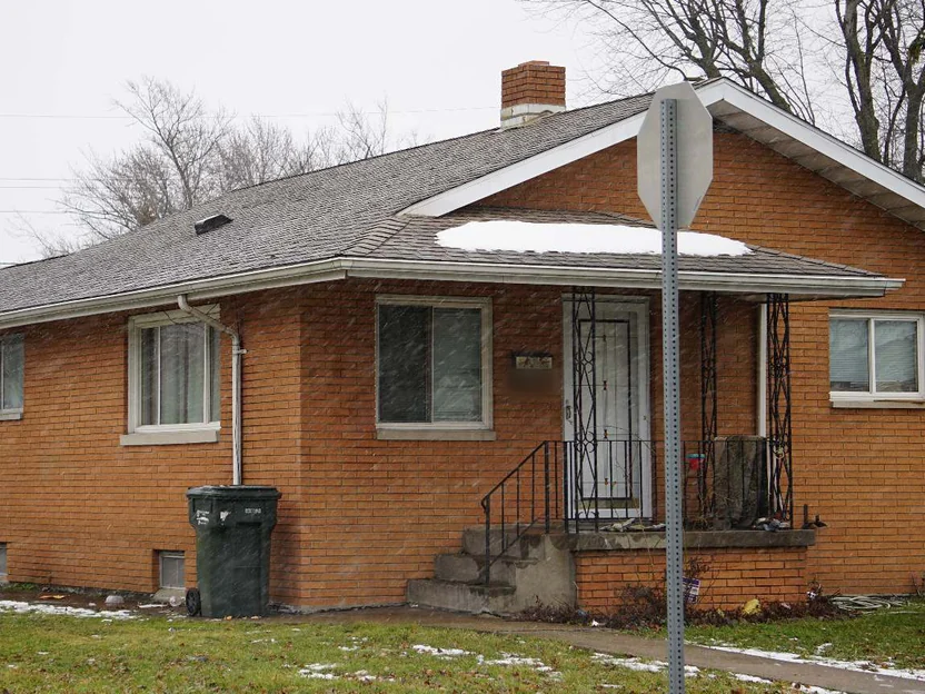 The front of the house in 2020 with snow falling, the rebuilt corner to the left of the porch steps carrying the same orange brick as the rest of the wall