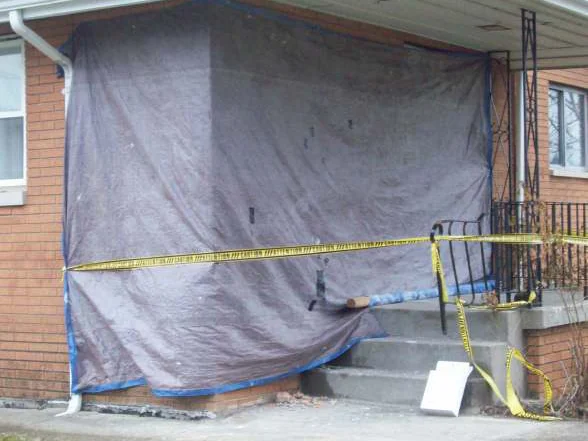 The corner of the house in 2010 wrapped in a grey tarp with yellow caution tape across the porch, before the brick was rebuilt