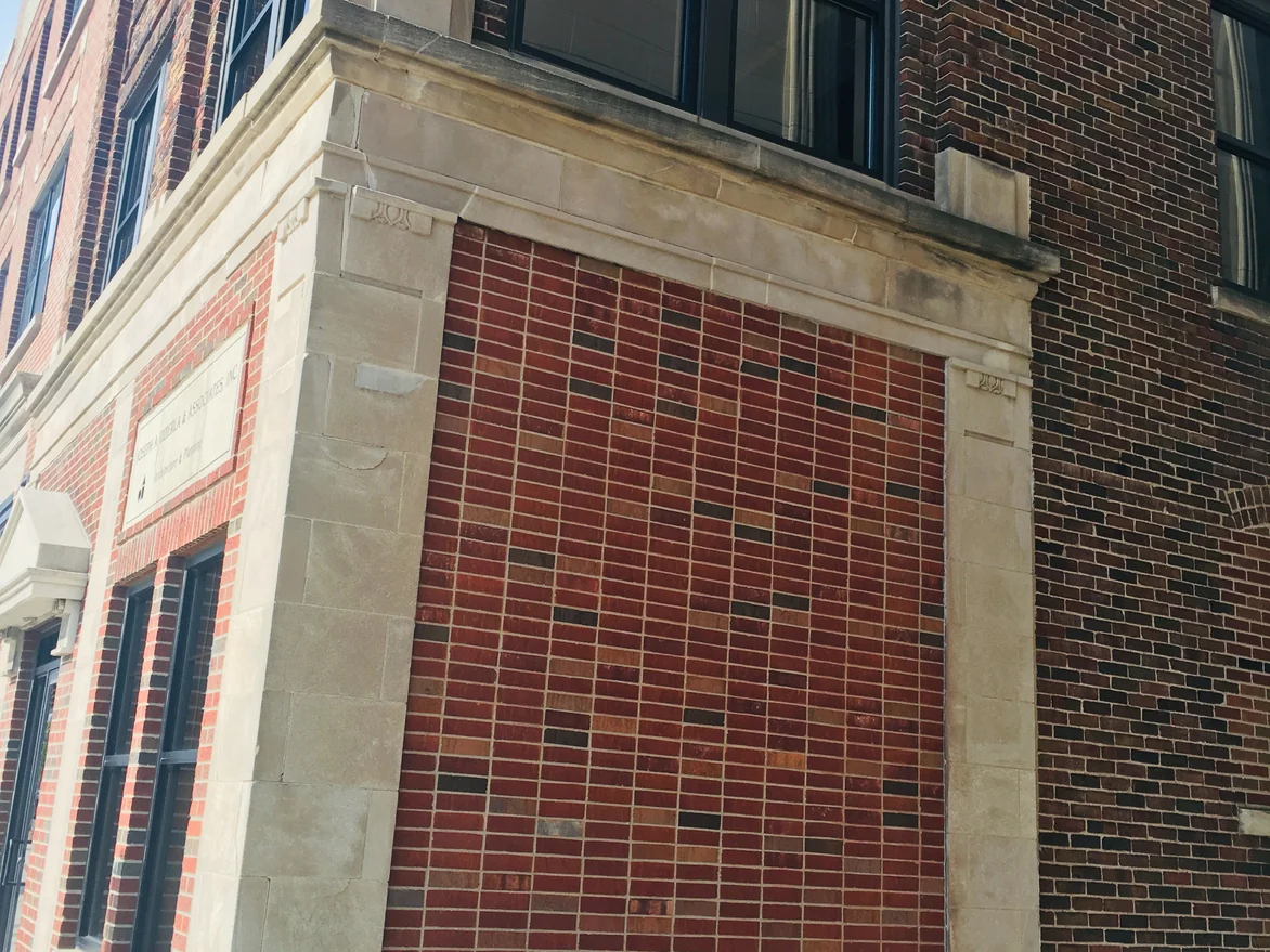 The alley elevation looked at from below in 2019, the blended brick running unbroken from the gas meter at the base to the limestone band above