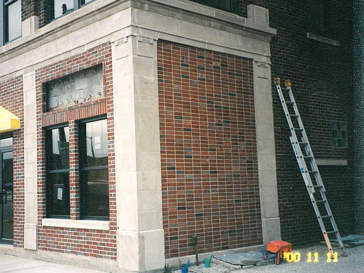The same corner with an extension ladder still standing against the alley wall, the pale and near-black units now blended into the brick around them