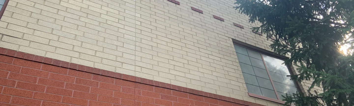 The school wall in 2019, a cream brick field over a red base band with a dashed accent course running through it
