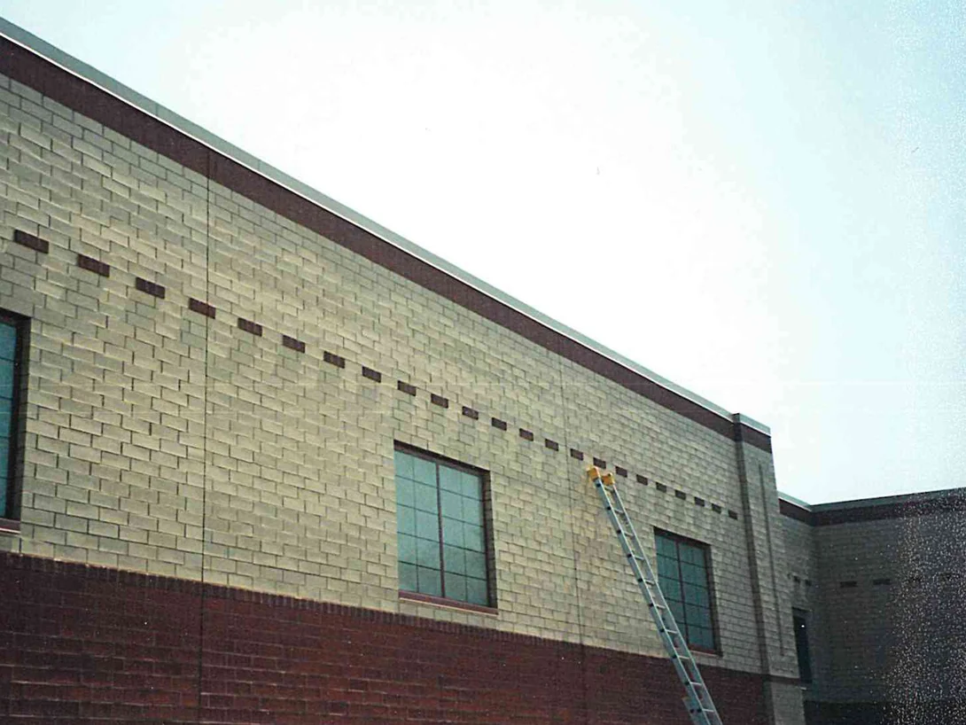 An extension ladder standing against the upper cream brick wall of the school, the dark base band running below it