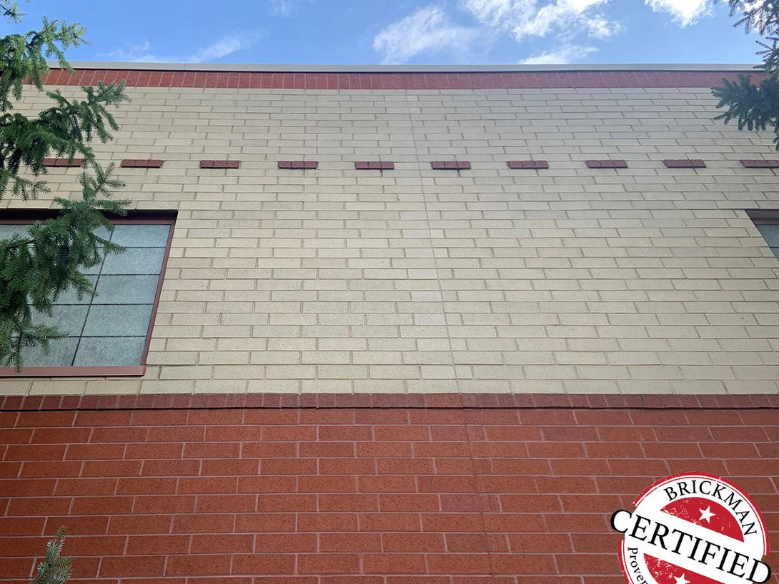 The stained wall photographed from below in 2019, cream brick over a red base band, carrying the Brickman Certified stamp
