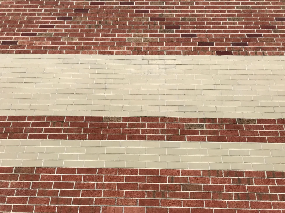 Red brick courses alternating with wide cream bands, seen at an angle along the wall in 2019