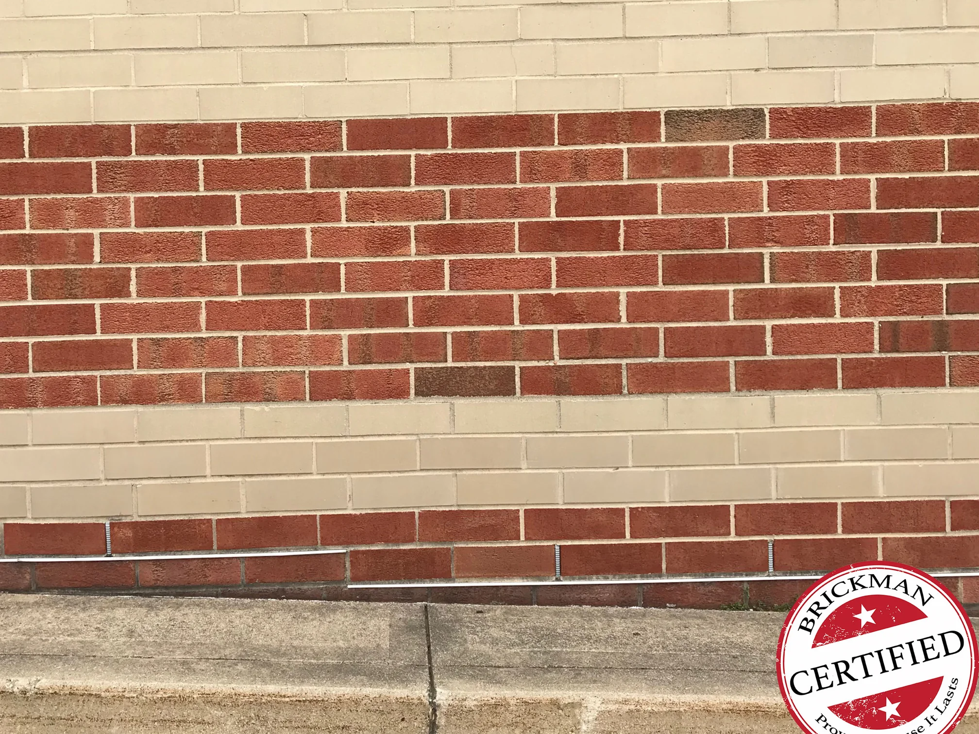 A banded wall at the pavement in 2019, a wide red band running between buff bands with no course reading out of range, the frame carrying the Brickman Certified stamp