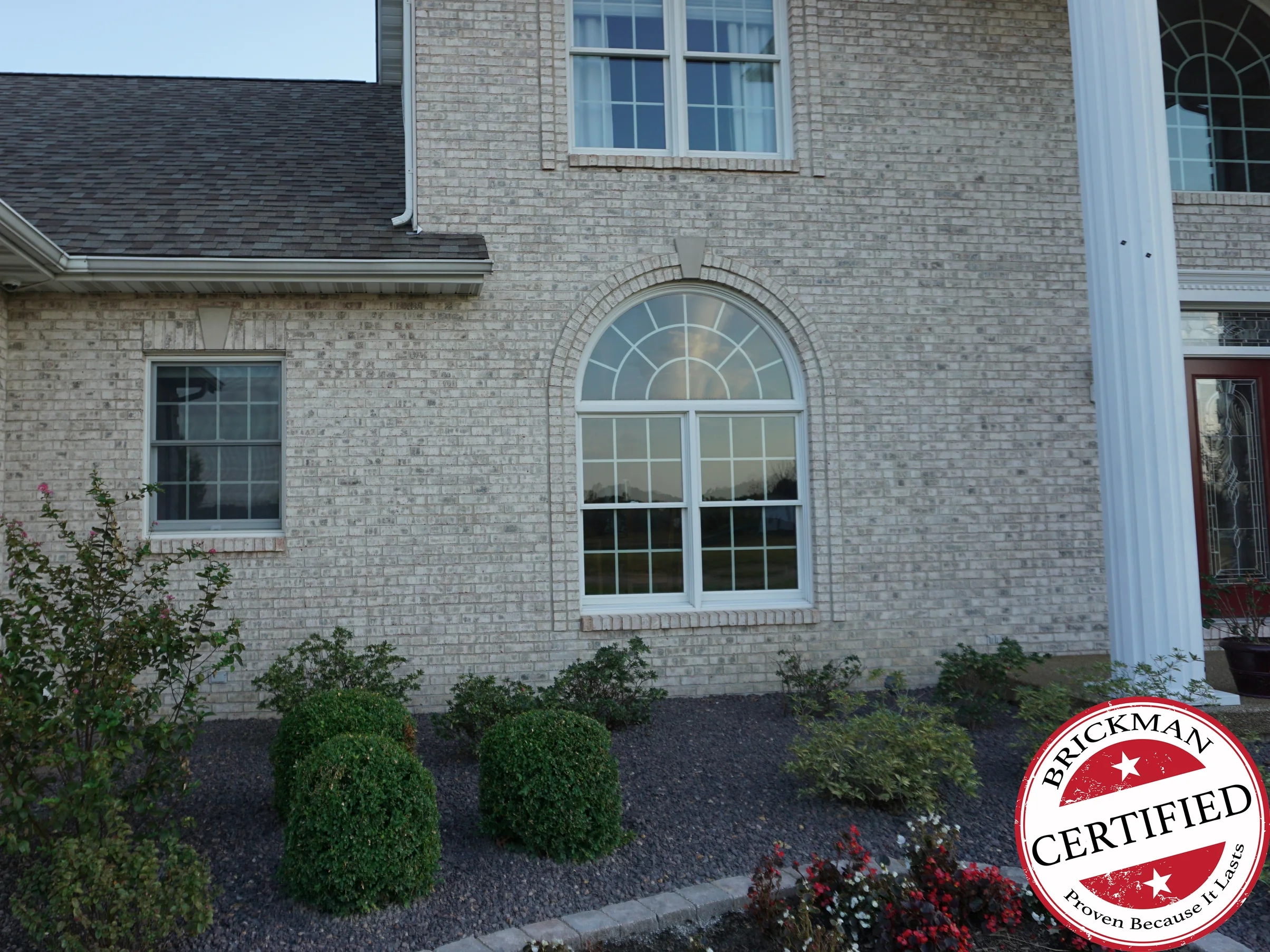 The front of the house in 2019, its cream and buff brick reading as one blend from the gravel bed to the eaves, with an arched window and a white portico column