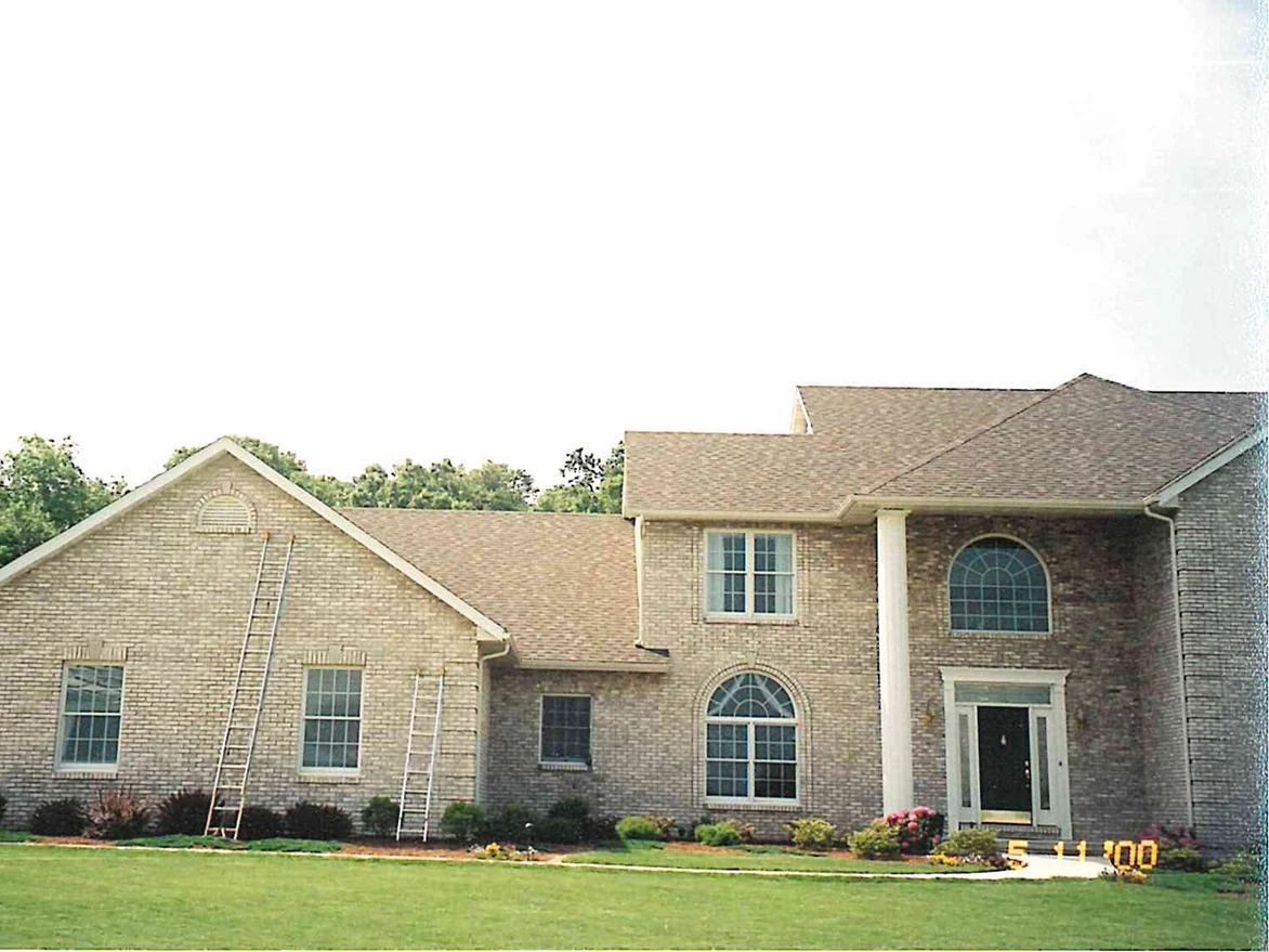 The whole front of the two-story house in 2000 with two ladders still standing against the left gable, its brick an even tan and cream across both wings