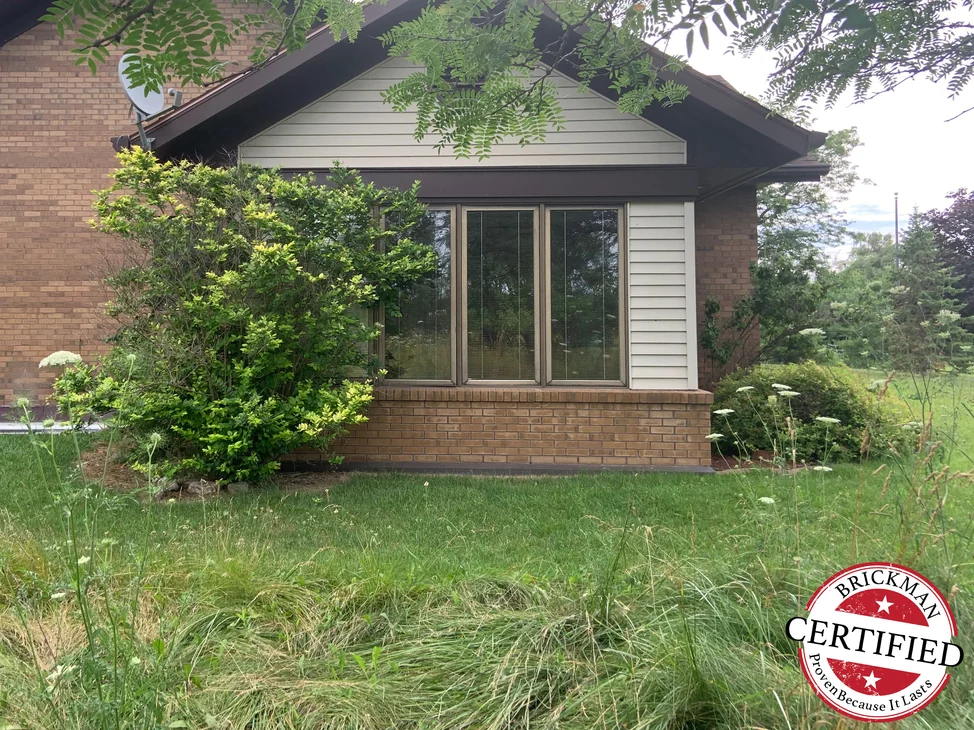 The gable end and glazed front bay of the house in 2019, the low wall under the windows reading the same brown range as the brick above it.