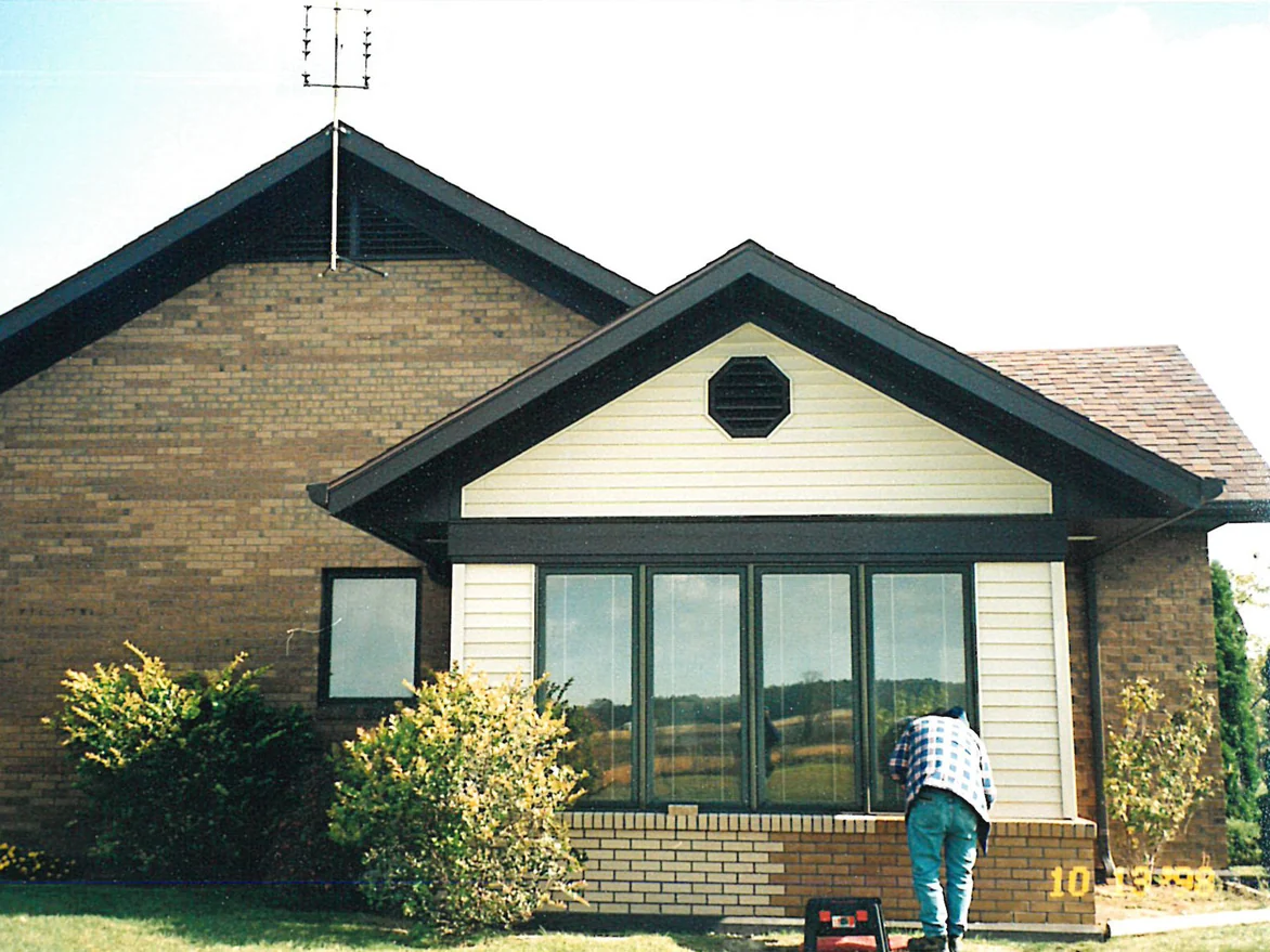 The front of the single-story house in 1998 with a man working at the low wall under the front windows, a toolbox on the grass and a camera date stamp reading 10 13 98 in the corner