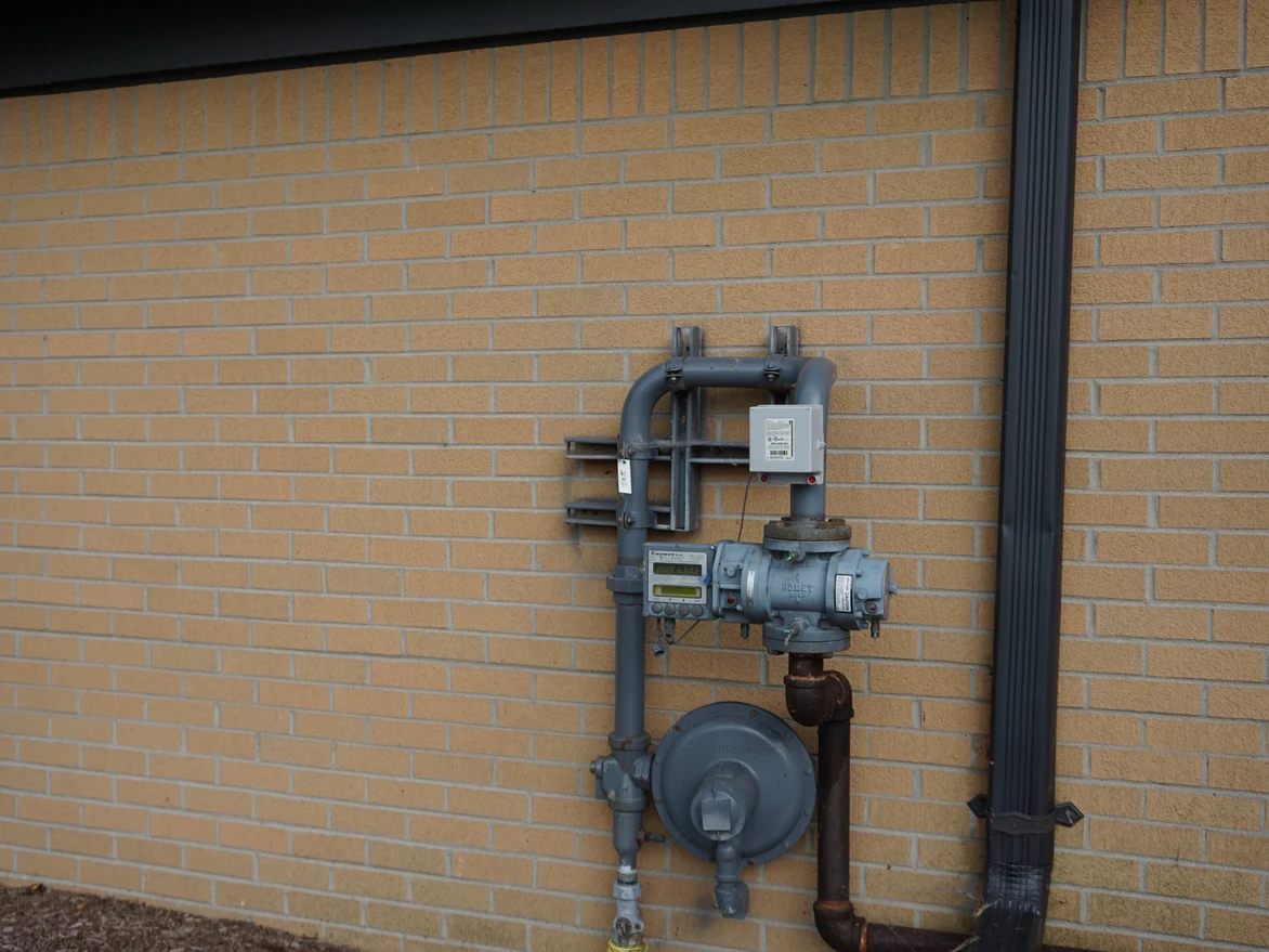 Close view of the buff brick at unit scale in 2019, a gas meter and riser mounted on the wall beside a downspout