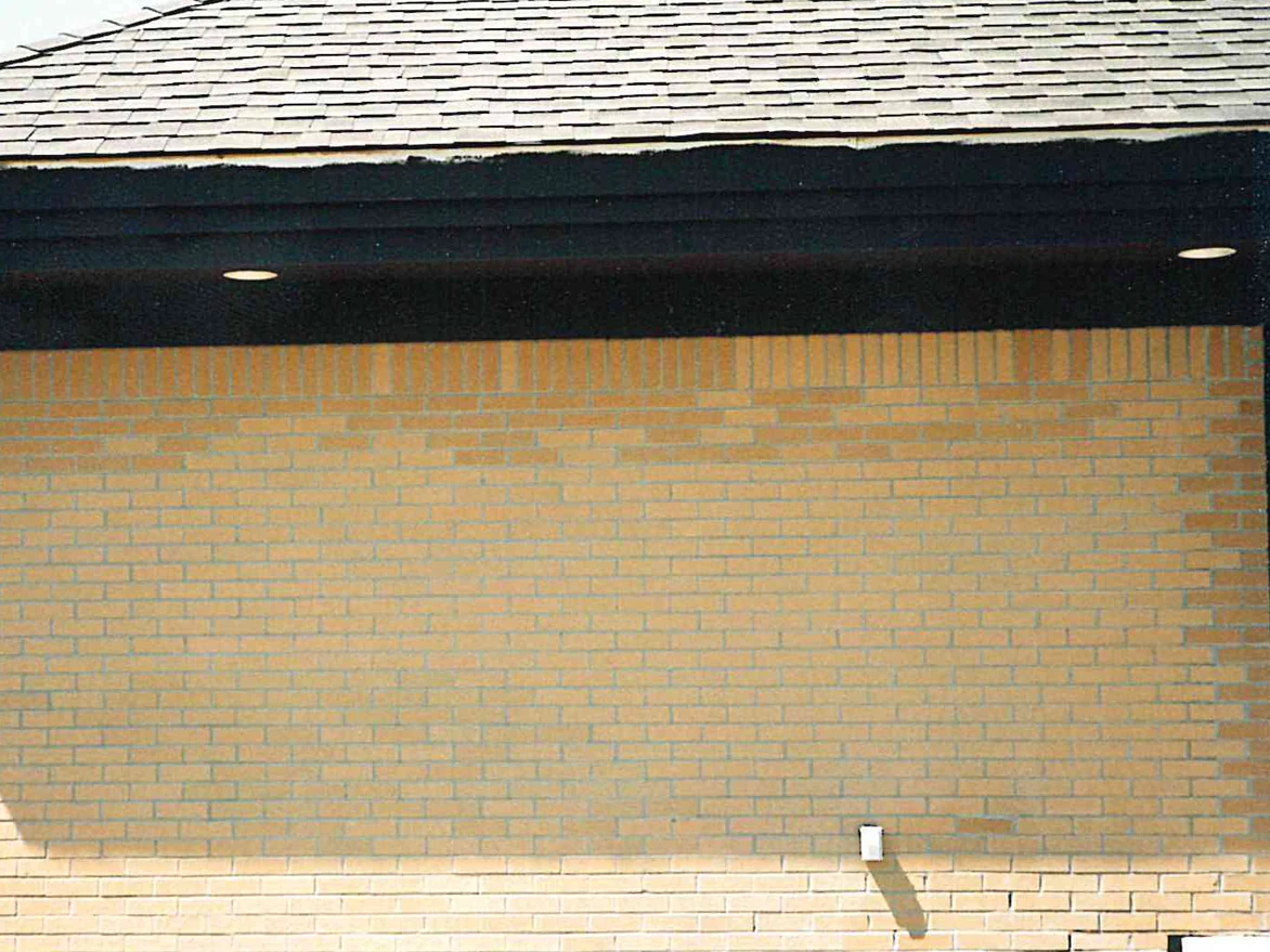 A long brick wall in 1998 with a band of noticeably darker orange units running across the top courses under the eaves, the brick below it a paler buff