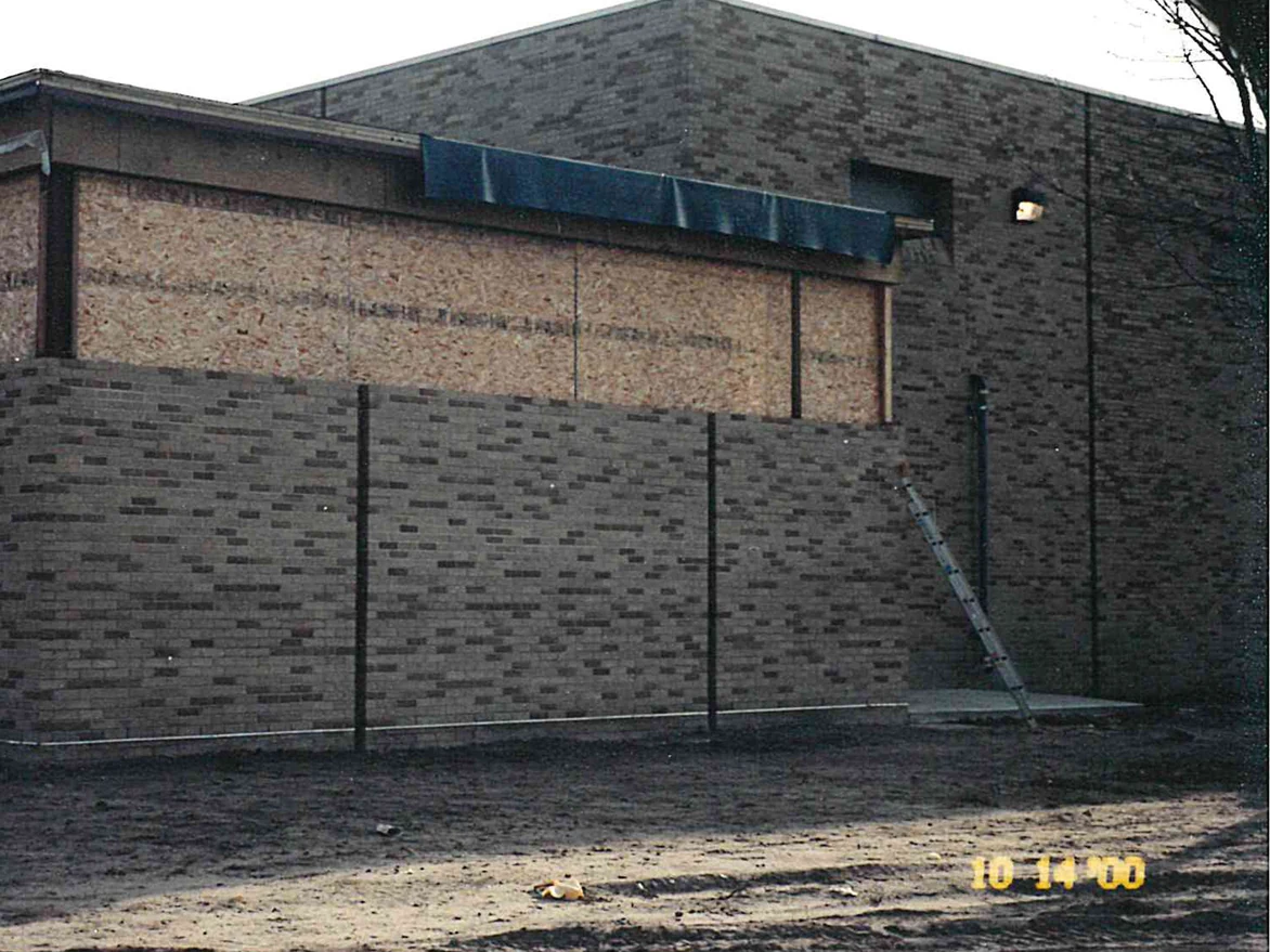 The same new wing later the same day, darker units now set through the light brick across the low wall, a ladder leaning at the far end