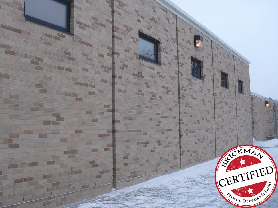 A long school elevation in 2019, light cream brick carrying scattered tan and brown units through it, punched windows down the wall and snow on the ground.