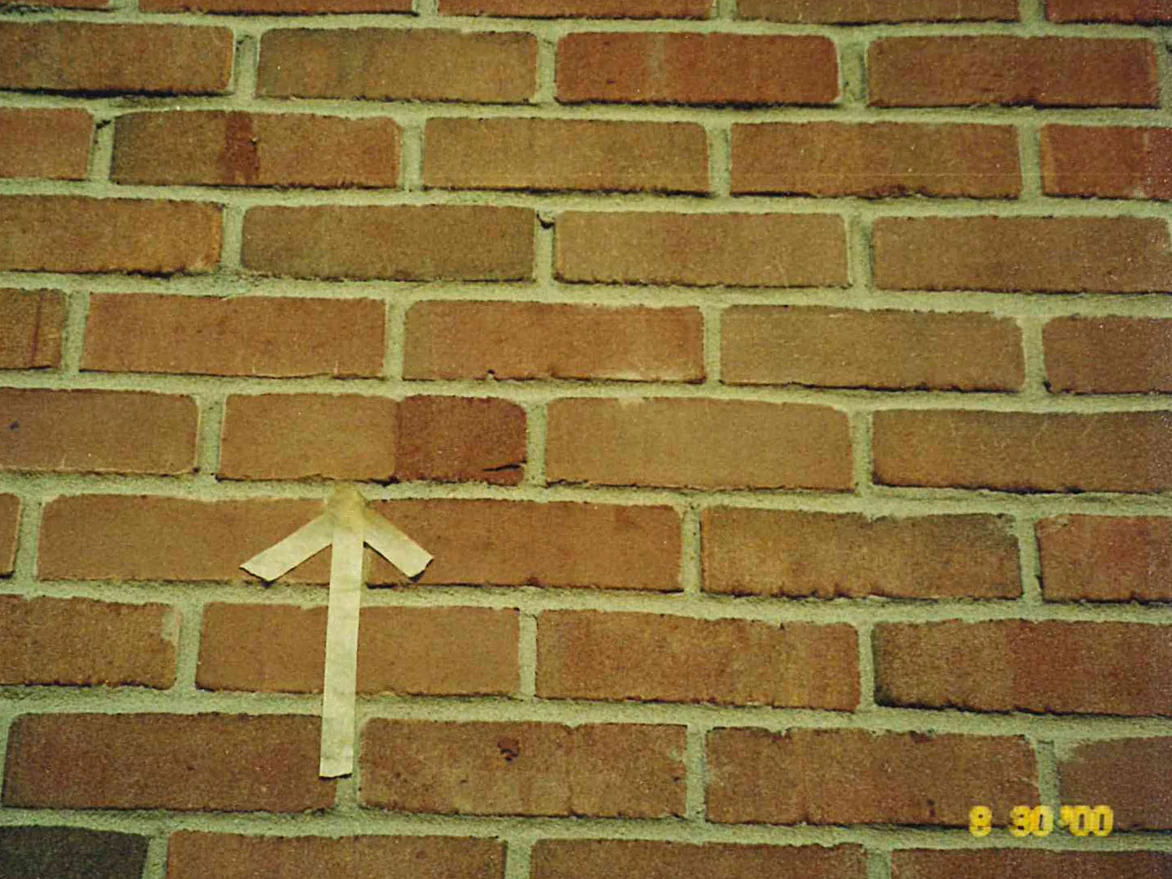 Close view of the house brick with a strip of masking tape folded into an arrow and taped up to point at one darker off color unit