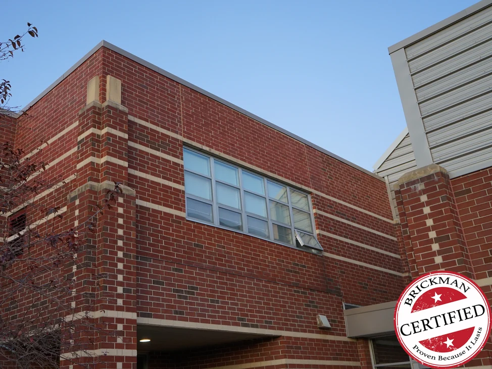 The school corner in 2019, red brick running one range with darker units set through it and cream limestone bands across the elevation.