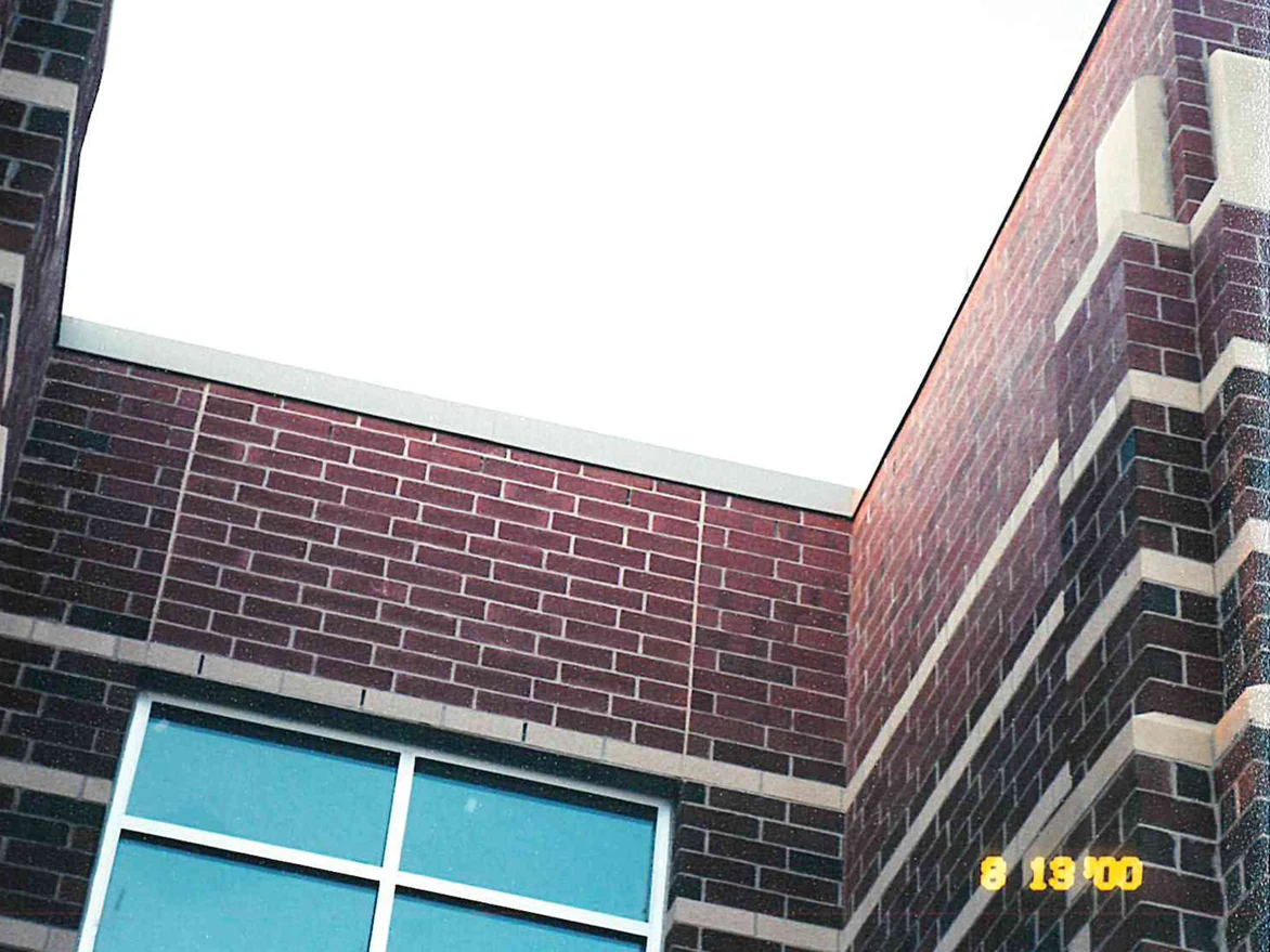 An inside corner of the school shot upward on the same day in 2000, the brick reading as one dark red and brown range to the parapet with cream limestone bands through it