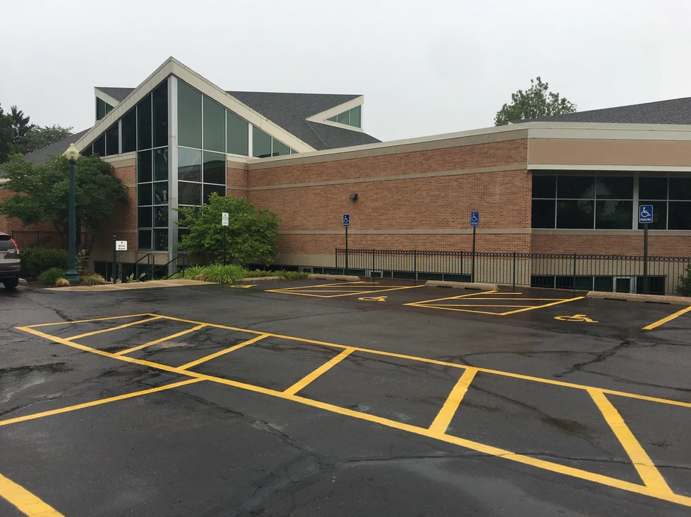 The church across its parking lot in 2019, the gabled glazed nave on the left and a long brick wing running away to the right