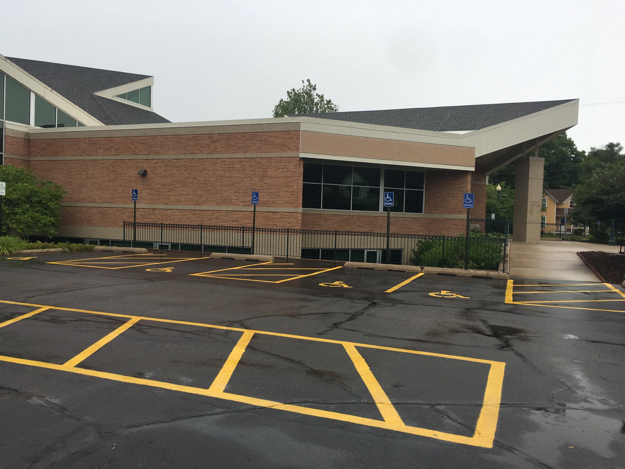 The covered entrance and the brick wing beside it in 2019, red brick banded in cream above an empty parking lot