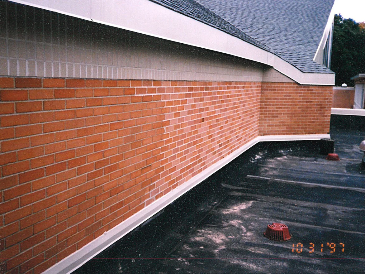 A brick wall running above a flat roof in 1997, a block of paler brick standing out from the orange red on either side of it