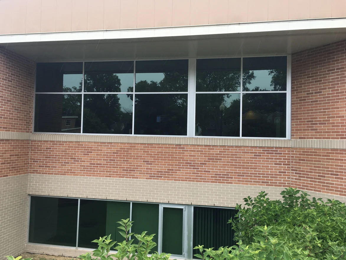 A band of windows under a soffit in 2019, red brick above and below it with courses of cream brick running through the wall