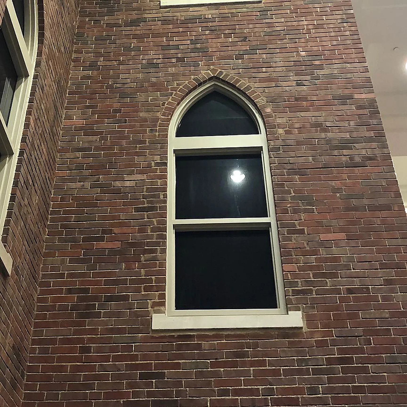The pointed arch window in 2019, photographed at night, the brick around its head and jambs now reading in range with the wall