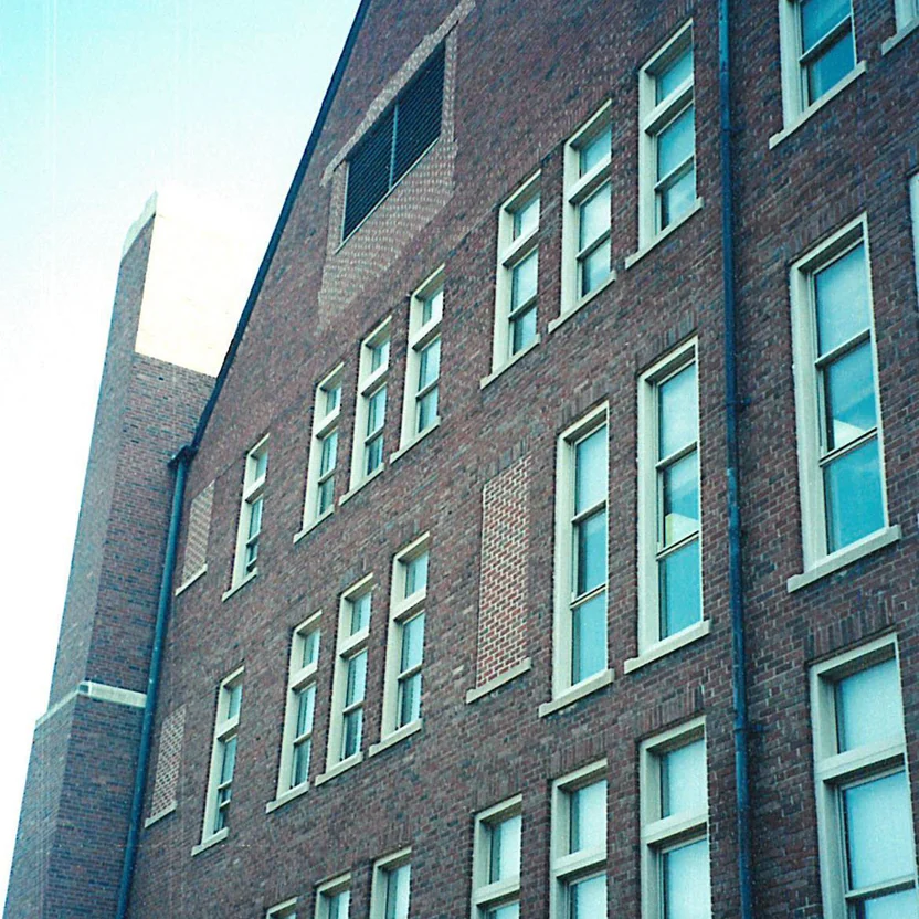A four-story brick elevation of the business school in 2000, shot from below, with pale rectangles of new brick between the windows where old openings were filled in, and a camera date of 5 10 00 in the corner