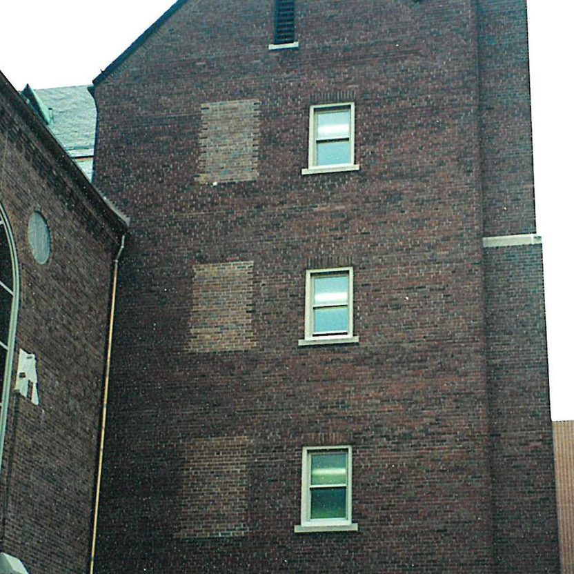 The gable end of the business school in 2000, three pale patches of new brick beside a column of windows where openings were filled in, a louvered vent under the peak