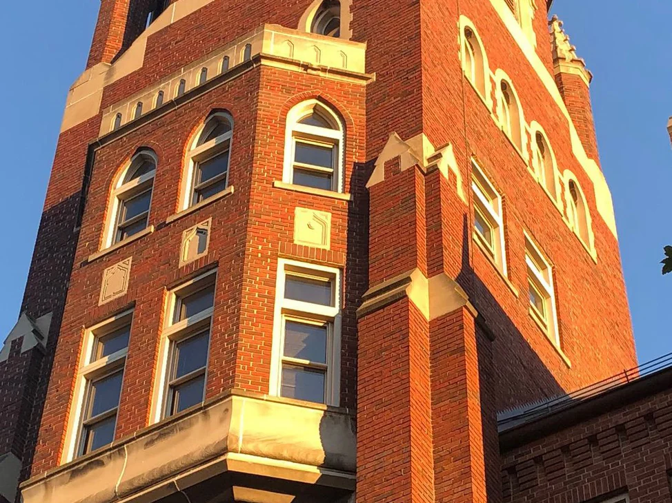 The brick tower of the St. Louis business school in 2020, arched windows and limestone bands in low evening sun, the brick reading as one range