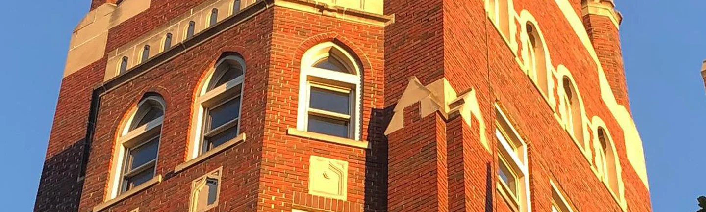 The brick tower of the St. Louis business school in 2020, arched windows and limestone bands in low evening sun