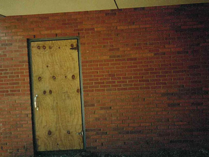 A wall beside a plywood-covered doorway in 1997, the brick mottled between dark and light units across the courses, with a camera date of 5/14/97 in the corner