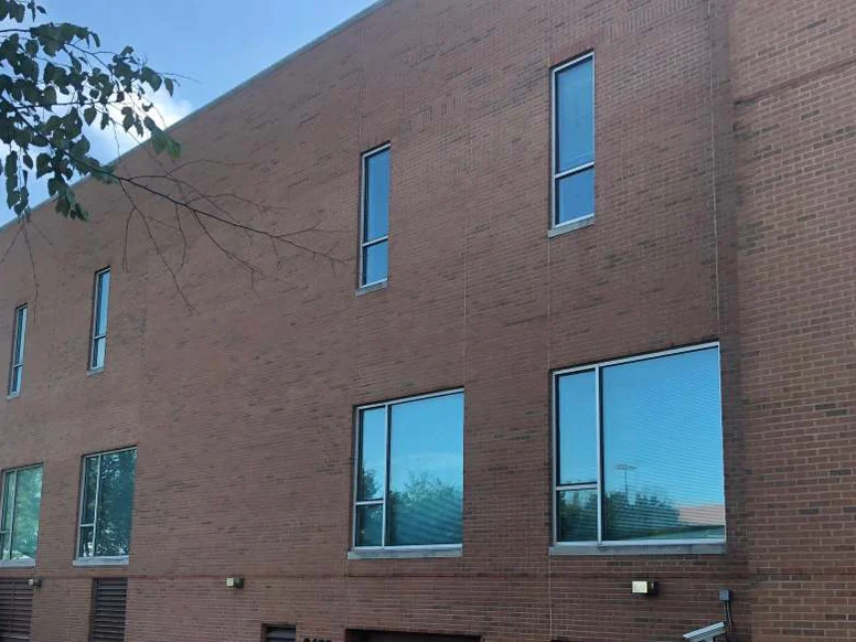 The three-story block in 2019, even red brick across all three floors, tree branches at the top left and cars in the lot