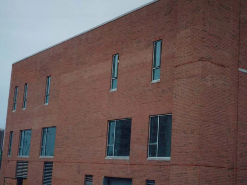 The three-story block in 1997 before staining, red brick with darker blotchy patches across the upper floors and a truck parked at the corner of the site