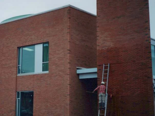 An applicator on an extension ladder against the red brick wall beside the tower in 1997