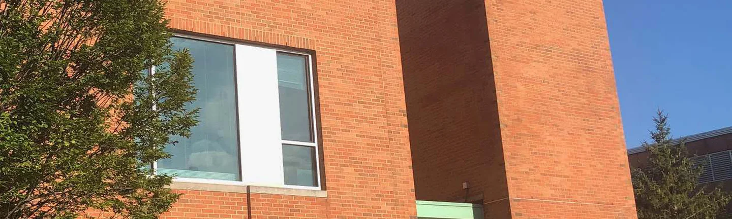 The brick tower of the university building in 2019, orange red brick under a green glass pyramid roof against a clear sky