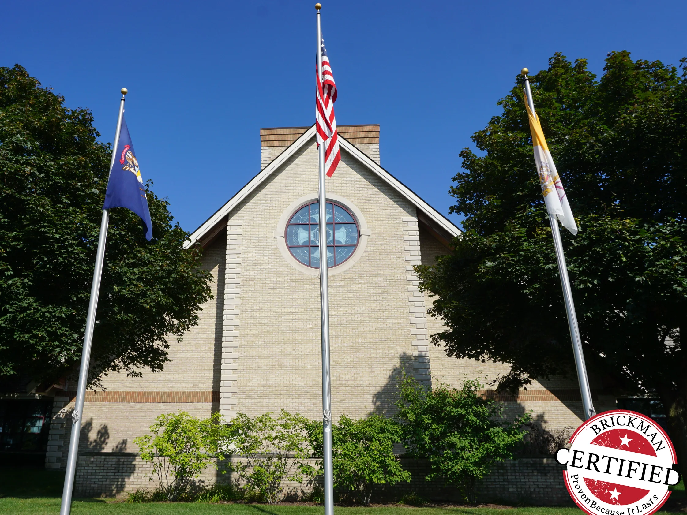 The church gable seen from the lawn in 2019, three flagpoles across the front and the brick reading as one even cream range