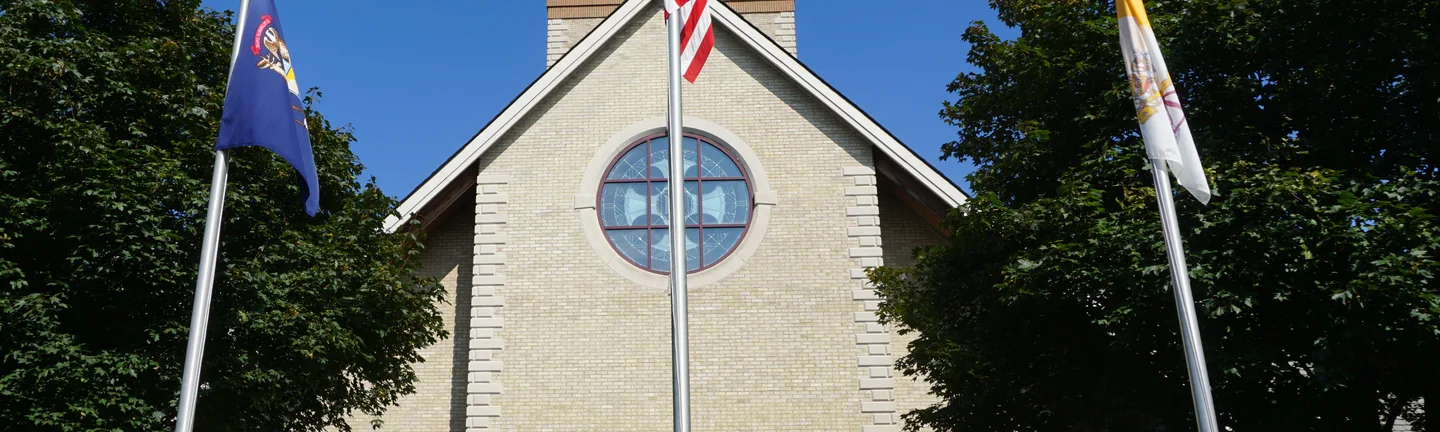 The church gable in 2019, its brick one even cream range behind three flagpoles