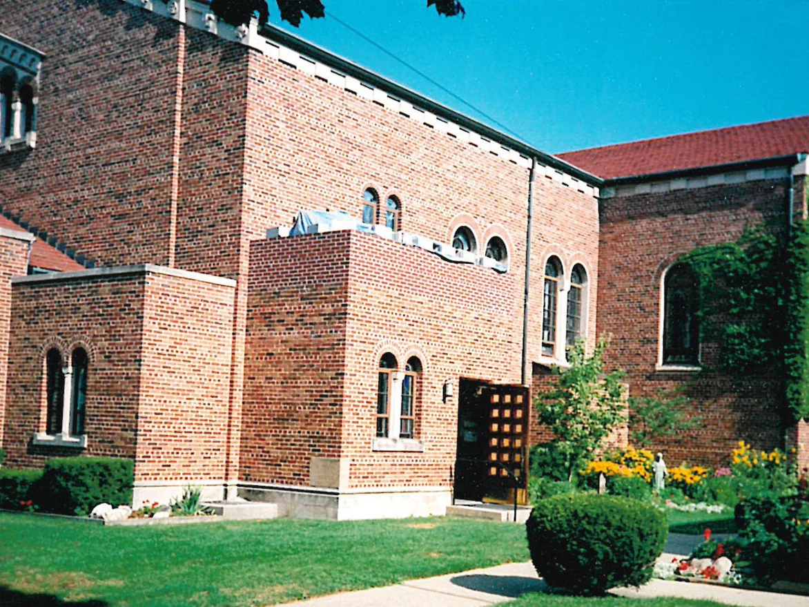 A new wing standing between two older parts of a brick church, its brick a pale pink against the darker original walls