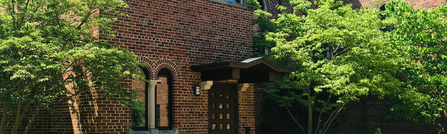 Brick wall of the church wing in 2019, with an arched window and the canopied entrance door