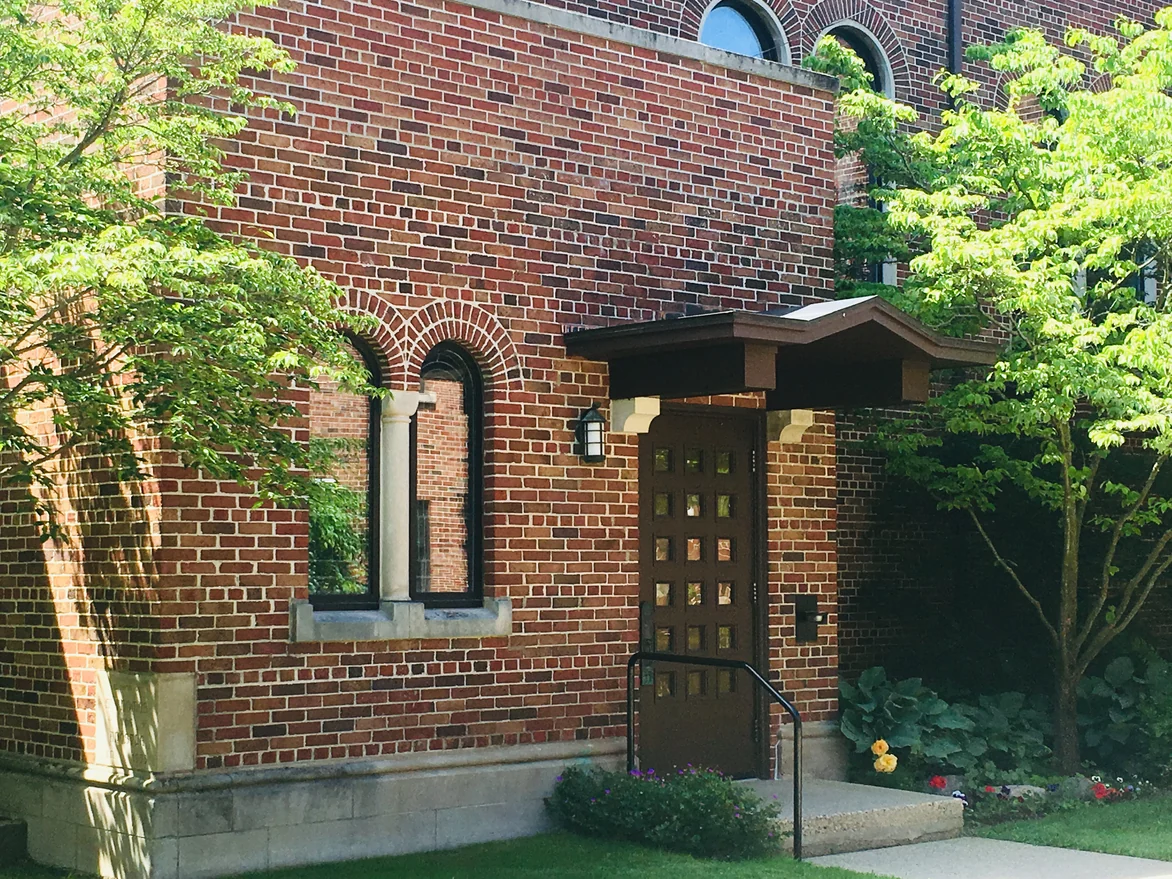 Close view of the wing entrance, a radiating brick arch over a twin window beside a canopied door, the units in mixed reds and browns