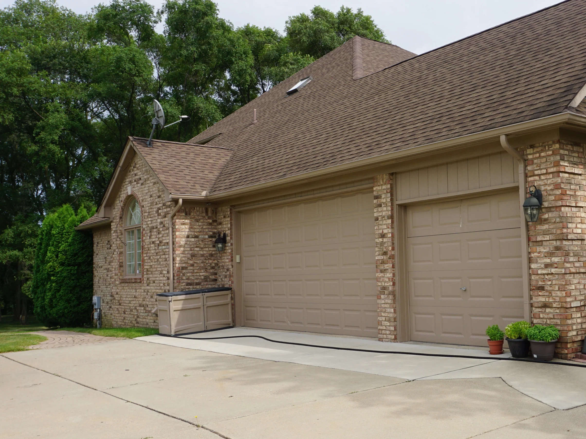 The house seen from the driveway in 2019, its brick one even tan and brown range across the gable end and the three garage bays